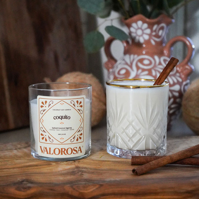 Coquito candle jar with a coquito drink on a wooden surface and vase in the background