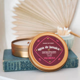 Candle in a tin with 'agua de Jamaica' label on a stack of books