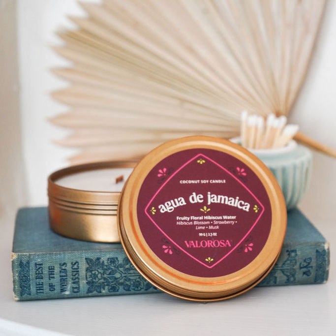 Candle in a tin with 'agua de Jamaica' label on a stack of books