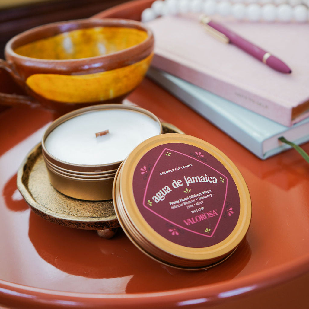 Candle in a decorative tin on a table with a notebook and pen in the background