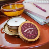 Candle in a decorative tin on a table with a notebook and pen in the background