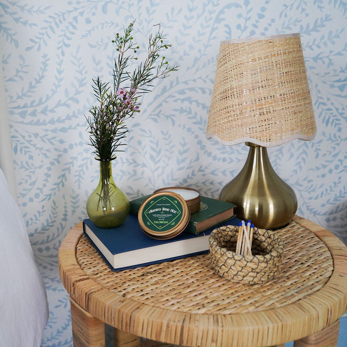 Wicker side table with decorative items against a blue patterned wall.