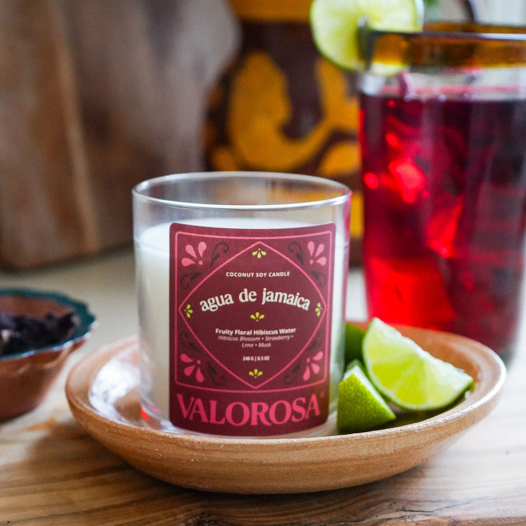 Candle labeled 'Valorosa' with a drink and lime on a wooden surface