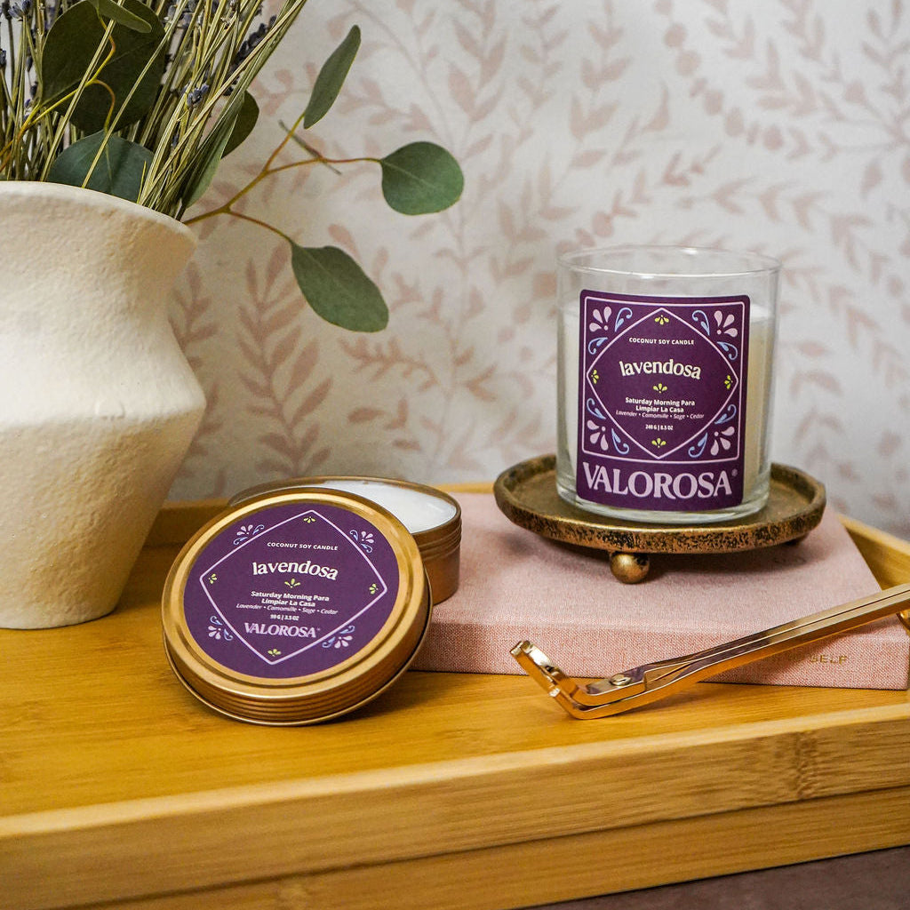 Valorosa Lavendosa candle jar and candle tin branding on a wooden surface with lavender and a vase in the background.