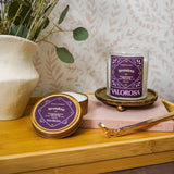 Valorosa Lavendosa candle jar and candle tin branding on a wooden surface with lavender and a vase in the background.