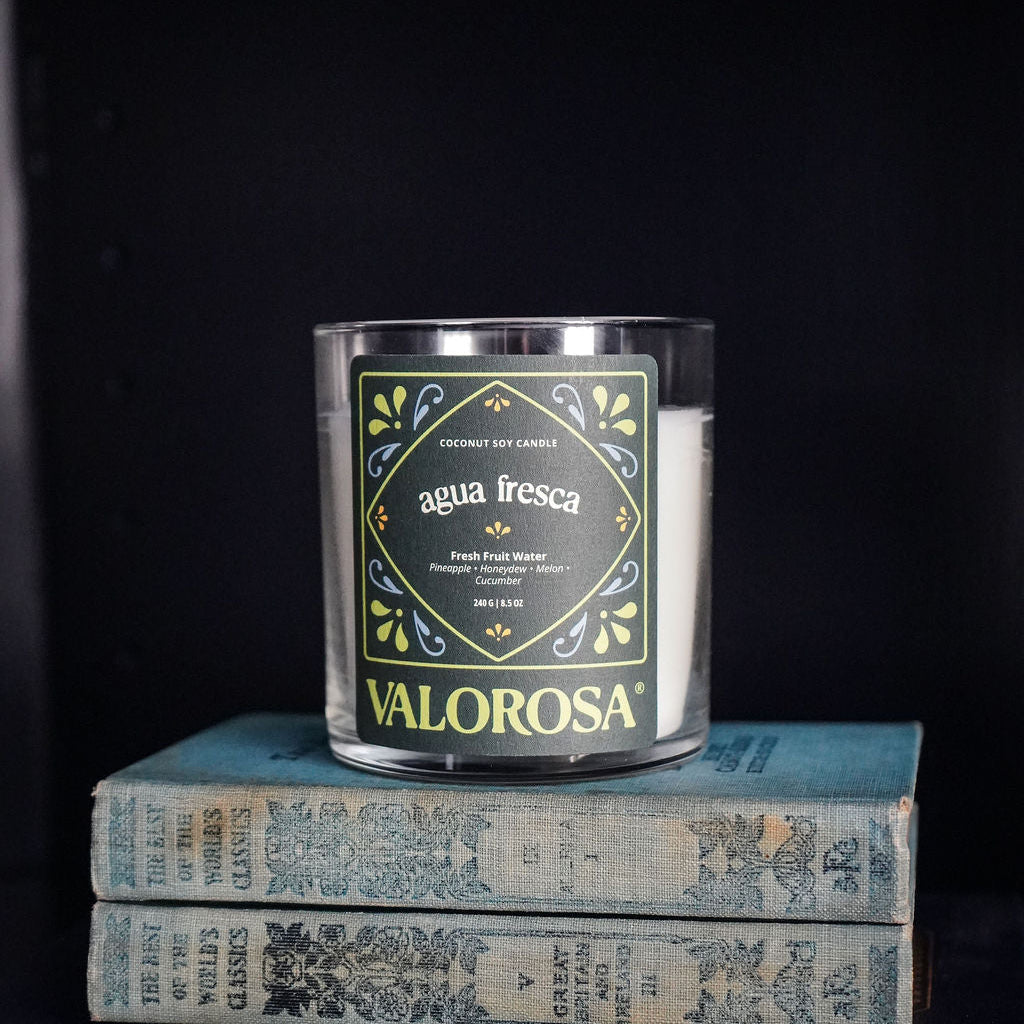 Valorosa Candle labeled 'Agua Fresca' on a stack of books with a dark background