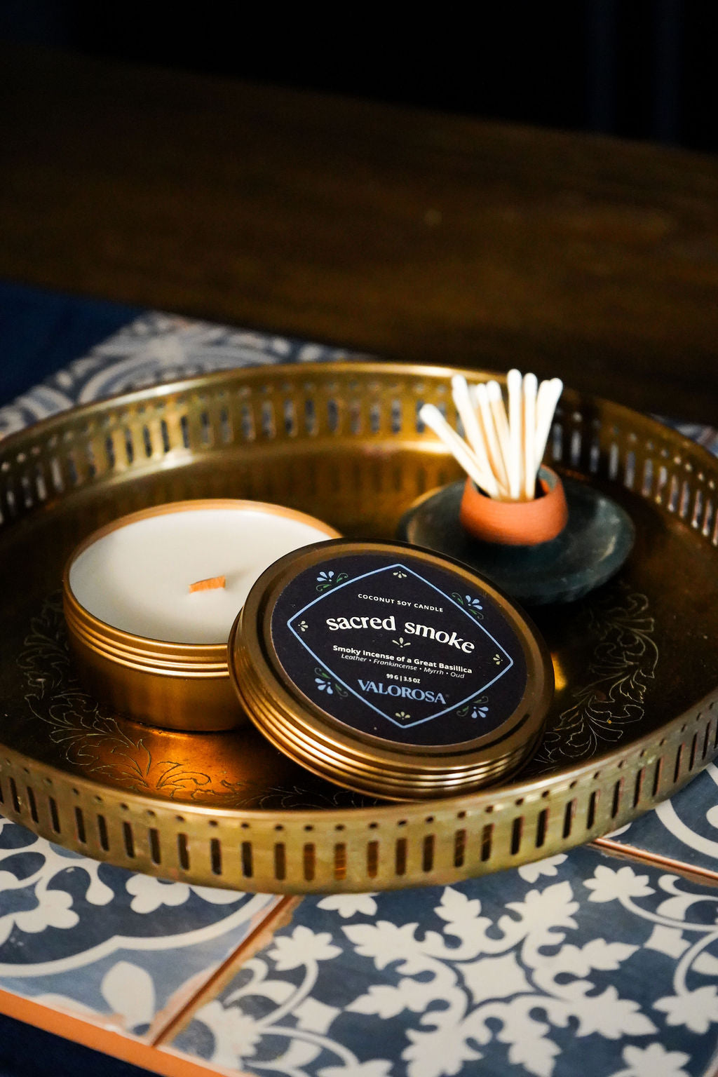 Sacred Smoke candle tin, incense stick holder, and on a decorative tray with a patterned surface.