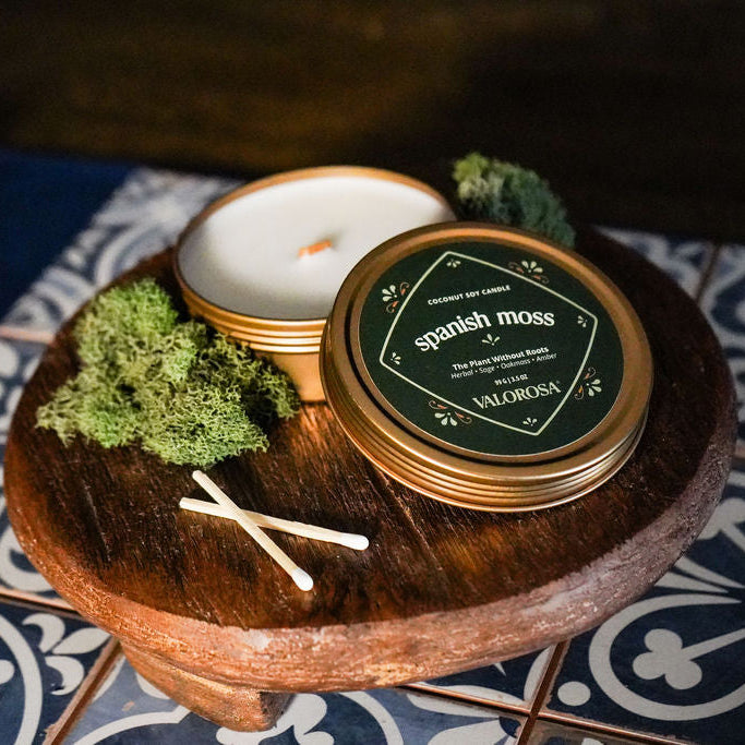 spanish moss candle tin with moss and matches on a wooden stand with a decorative background