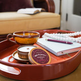 Red tray with a valorosa agua de jamaica candle, cup, saucer, and small containers on a couch in a living room.