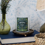 Valorosa candle labeled 'Agua Fresca' on a table with a vase, books, and lamp.