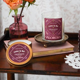 Como La Flor Candle Jar and Candle Tin on a wooden table with flowers and books.