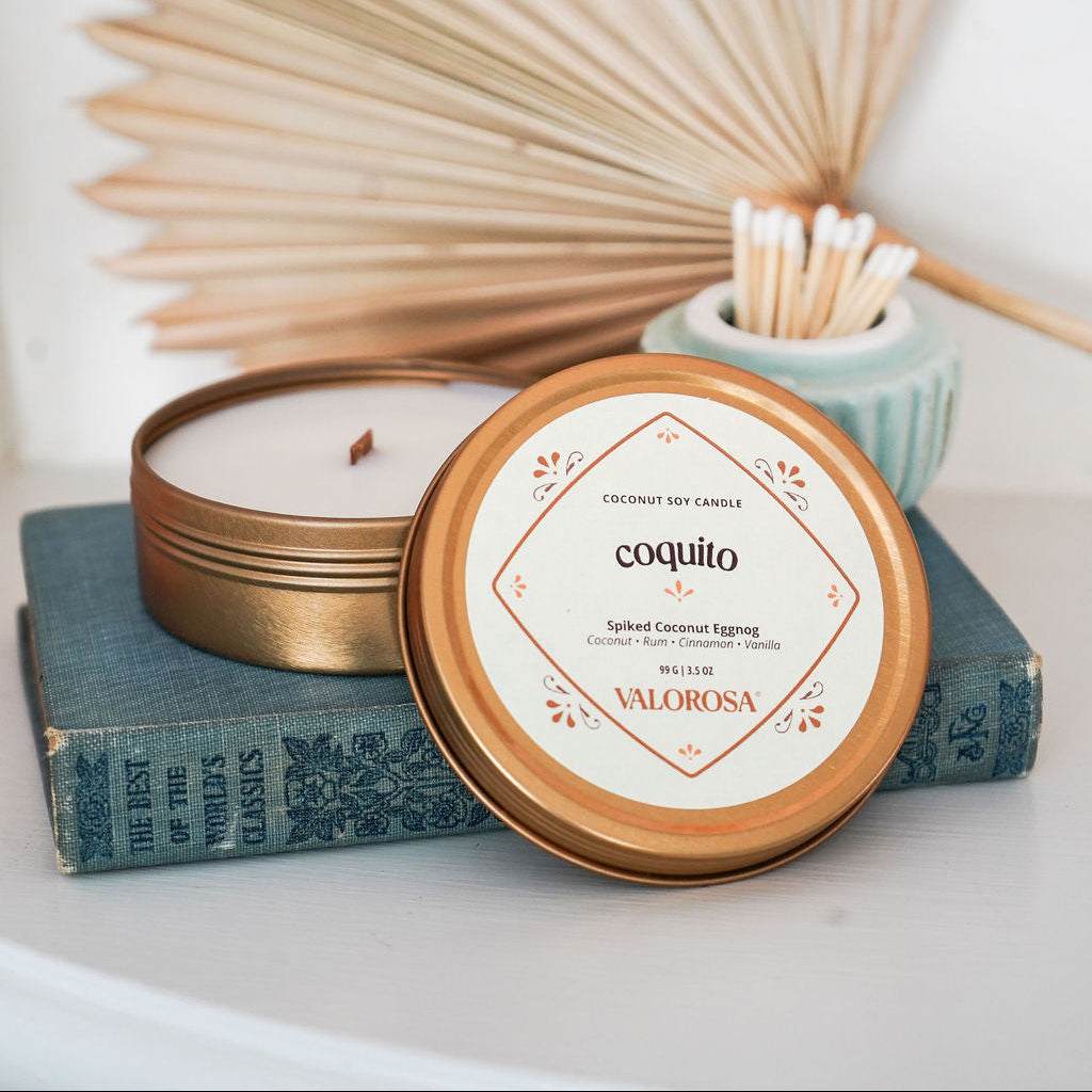 Coquito Candle with a decorative lid on a white surface with dried leaves and books in the background