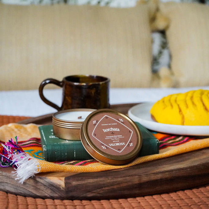 Tray with a yellow cake, mug, and horchata candle on a textured surface with pillows in the background