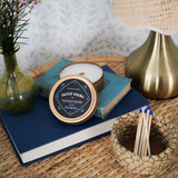Decorative setting with books, a sacred smoke candle tin and a lamp on a textured surface.